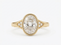 Top-down view of a 3 CT oval lab grown diamond set in a yellow gold full bezel ring with pave cluster band accents.