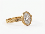 Angled view of a 3 carat oval lab grown diamond bezel ring in yellow gold with vintage filigree engraving.
