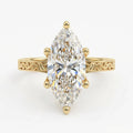Top-down view of a 4 CT marquise cut lab grown diamond solitaire engagement ring with 6 prongs and engraved yellow gold band.