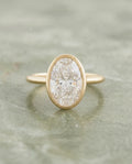    Top-down view of a 2 CT oval cut lab grown diamond engagement ring in a yellow gold bezel setting with milgrain trim.
