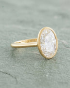 Side angled perspective view of a 2 carat oval bezel set lab diamond ring in yellow gold.