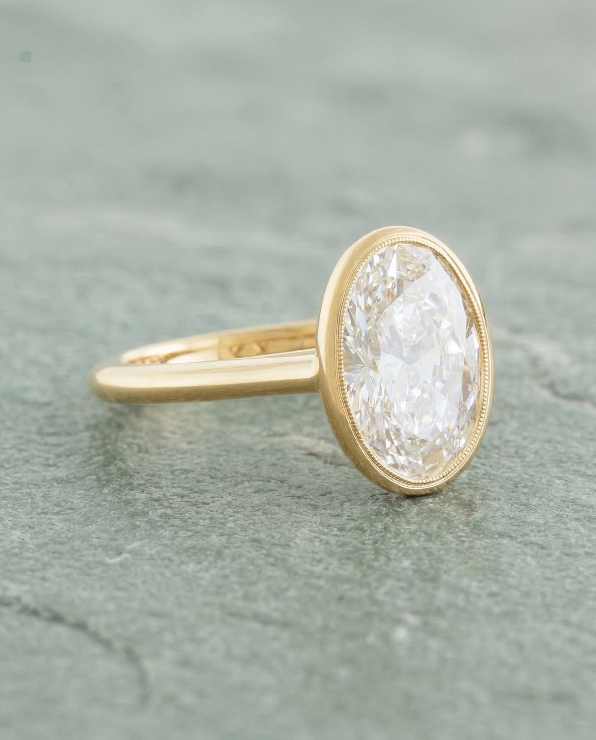 Side angled perspective view of a 2 carat oval bezel set lab diamond ring in yellow gold.