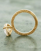 Angled perspective view of a 4 CT oval cut lab grown diamond engagement ring with pavé band and textured claw prongs in yellow gold.