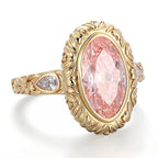 Angled view of a 4 carat blush pink oval lab grown diamond ring framed by a sculpted leaf bezel and pear side accents.