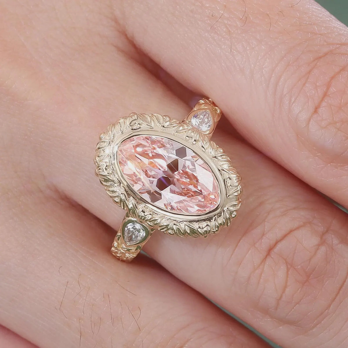 Close-up on-finger view of a 4 CT pink oval lab grown diamond engagement ring with vintage carved floral frame.