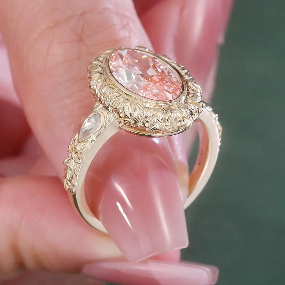 High-angle perspective on hand showing the botanical engraved bezel and center pink oval diamond.