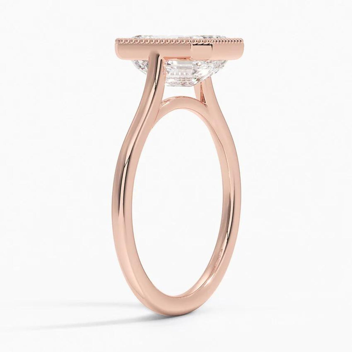Three-quarter profile view of a 4 CT emerald cut lab grown diamond engagement ring with milgrain bezel frame in rose gold.