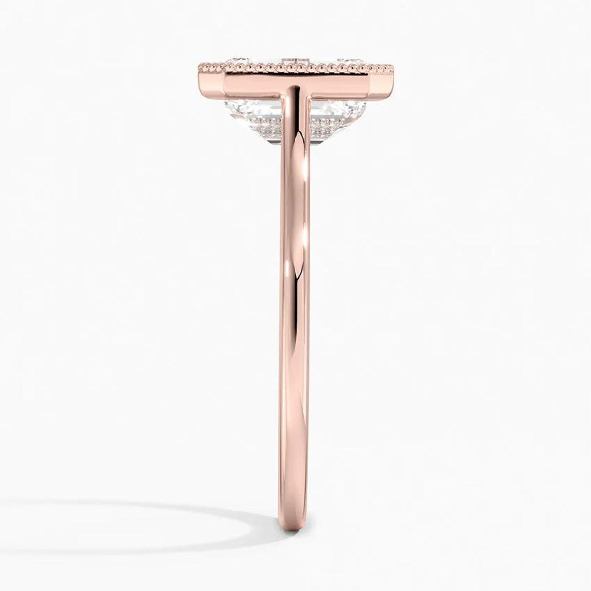 Direct side profile view showing the slender rose gold band and milgrain frame setting of an emerald cut diamond ring.