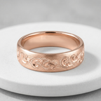 Studio shot of a men's carved scroll rose gold wedding band displayed on a white marble pedestal.   