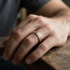 Lifestyle view of a man wearing a vintage carved rose gold wedding band resting his hand on a rustic wooden table.
