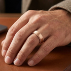 On-hand view of a man wearing a rose gold brushed wedding band with textured edges.