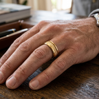 Close-up lifestyle photo of a man's hand wearing a yellow gold pyramid stud band at a wooden desk