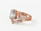 Perspective side angle of a rose gold 3 ct oval lab diamond ring stacked with a matching leaf-detailed curved wedding band.