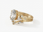 Side angle view of a 14k yellow gold 3 ct oval lab grown diamond engagement ring with a matching contoured chevron leaf band.