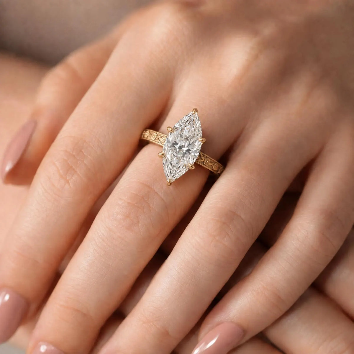 Close-up on hand showing a 3 carat marquise cut lab diamond set in a vintage floral relief yellow gold band.