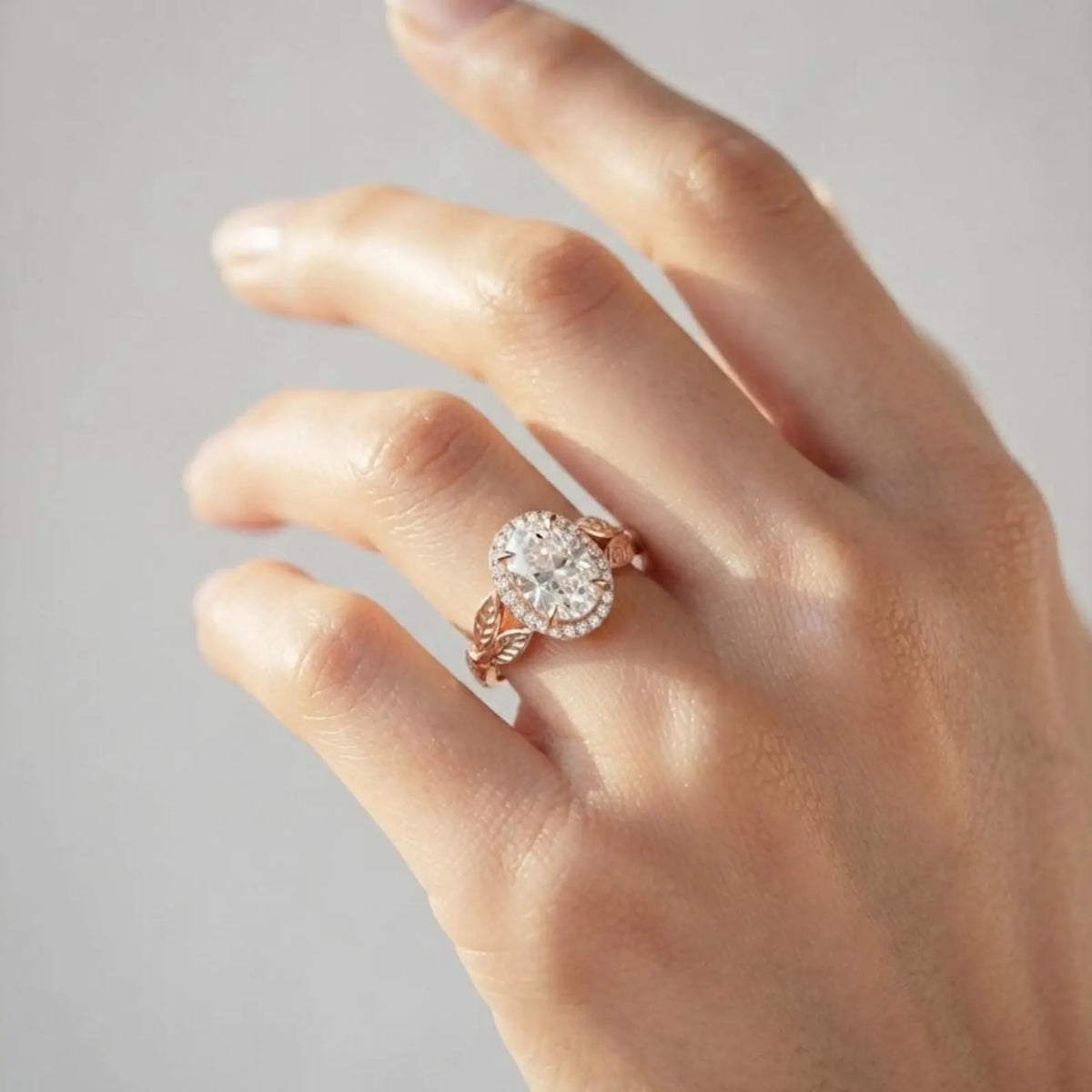 On-hand view of a 2 CT oval lab grown diamond halo engagement ring in rose gold with sculpted leaf shoulders.