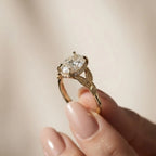 Hand holding a yellow gold 2 CT oval cut lab diamond halo engagement ring highlighting the leaf motif shank.