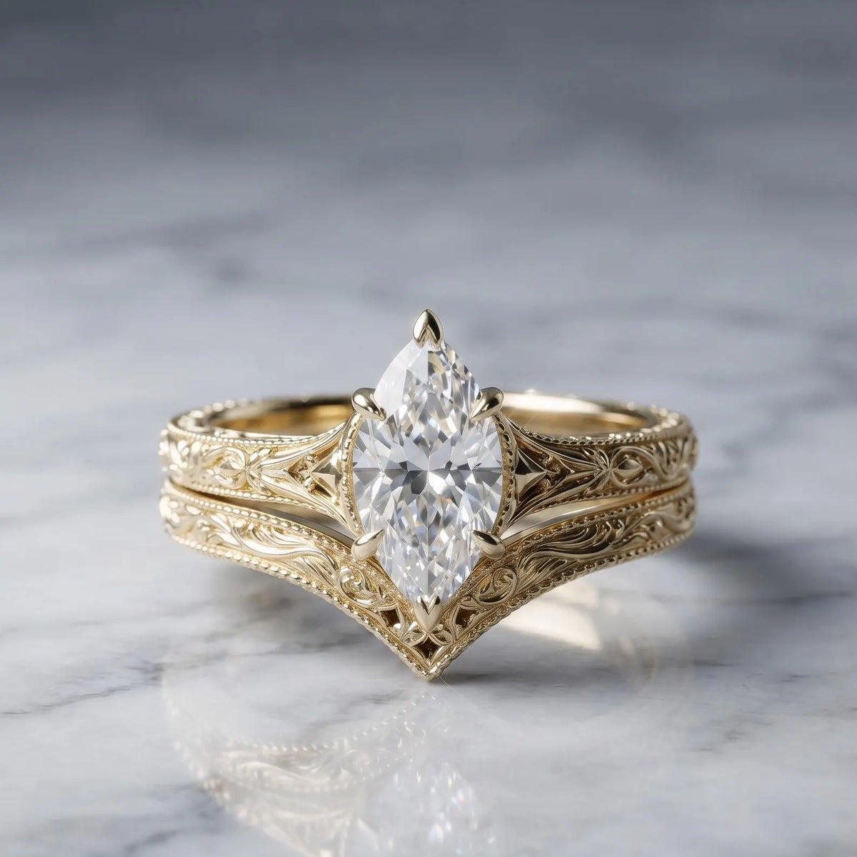 Studio view on marble of a 2 CT marquise lab grown diamond engagement ring with a matching vintage floral engraved curved chevron band in yellow gold.