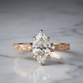 Studio shot on marble of a 3 CT marquise lab grown diamond ring in rose gold with vintage scrollwork band.