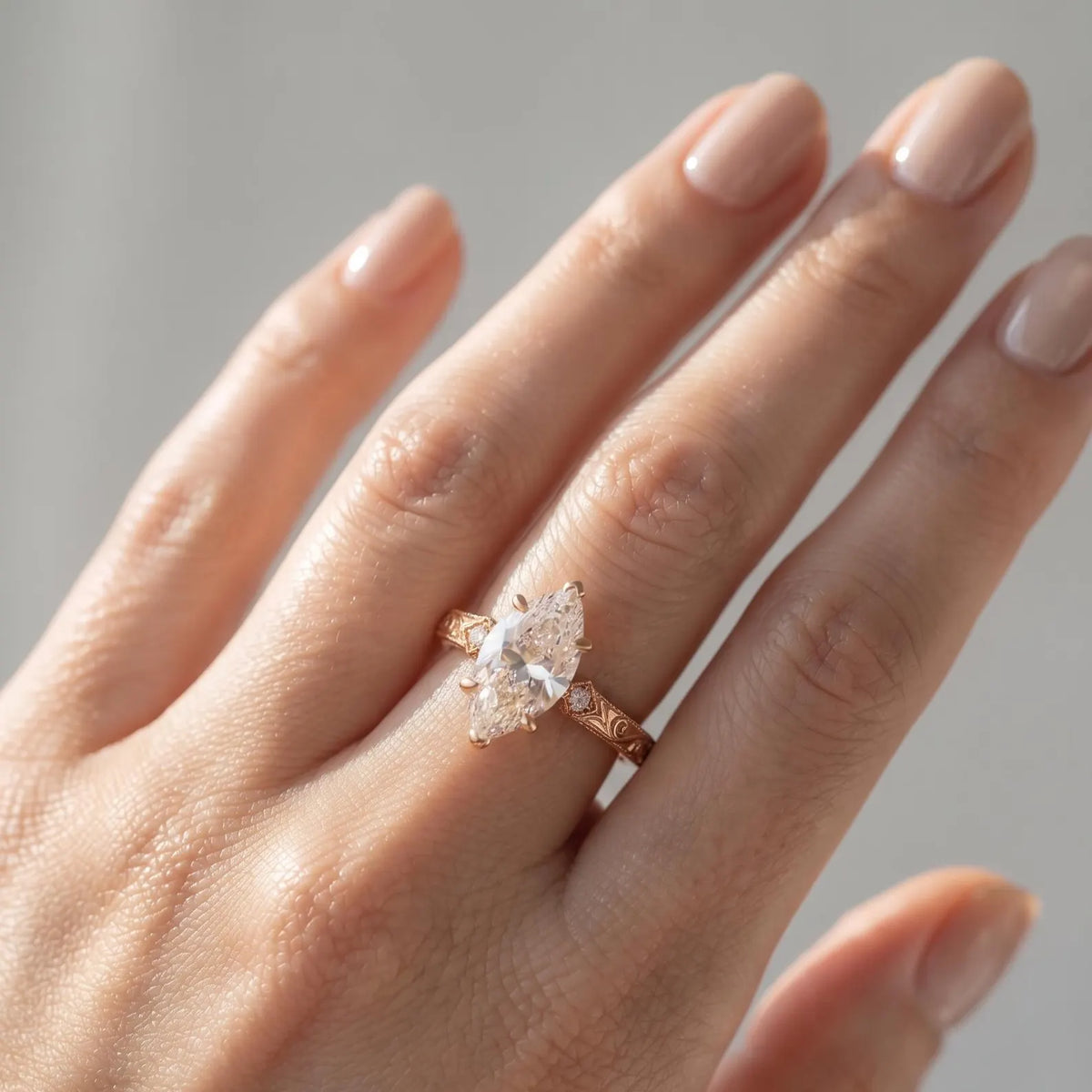 Top-down view on hand showing a 3 CT marquise lab grown diamond ring with filigree engraved rose gold band.