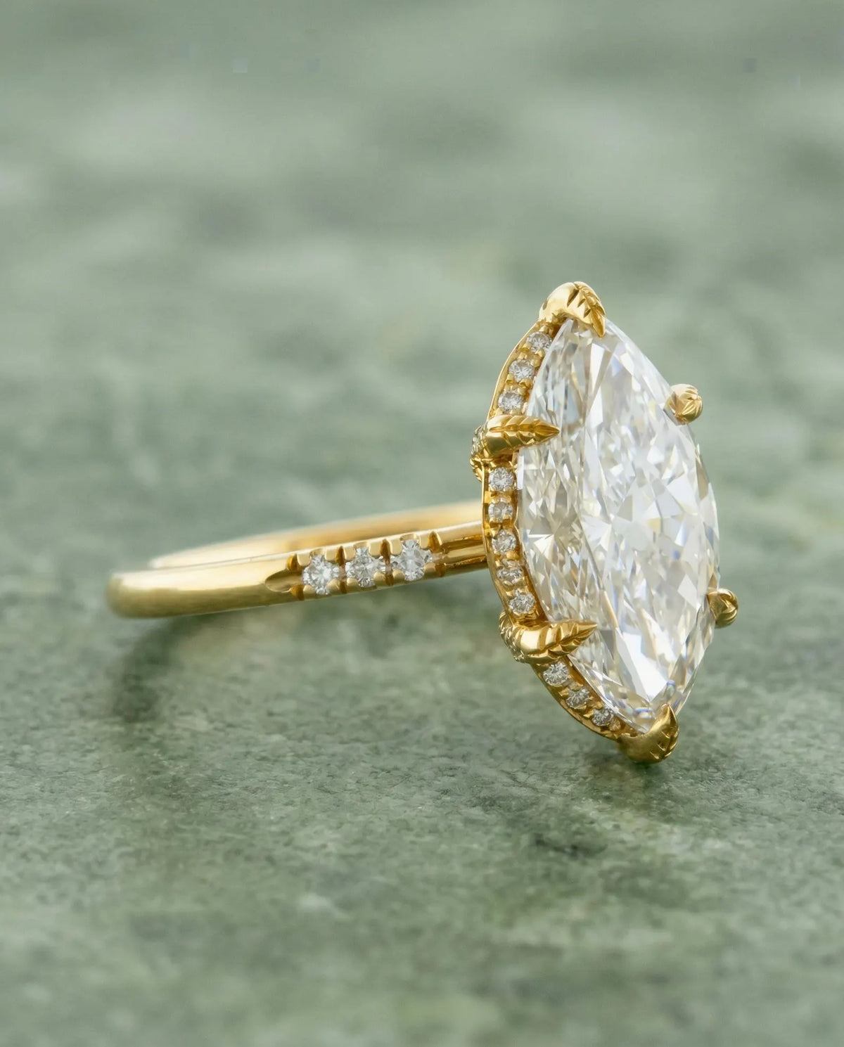 Three-quarter profile view of a 4 CT marquise lab grown diamond ring in yellow gold with leaf-textured prongs and hidden halo.