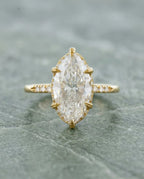 Top-down view of a 4 CT marquise lab diamond engagement ring held by six leaf-engraved yellow gold prongs.
