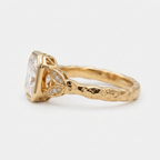 Side profile of a 3 CT radiant cut lab grown diamond bezel ring in yellow gold with leaf accents and hammered band texture.