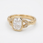 Angled view of a 3 CT radiant cut lab diamond bezel ring with pave leaf side accents in yellow gold.
