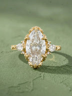 Top view of a 4 CT marquise cut lab grown diamond engagement ring in yellow gold featuring claw prongs, pear side stones, and an engraved band.