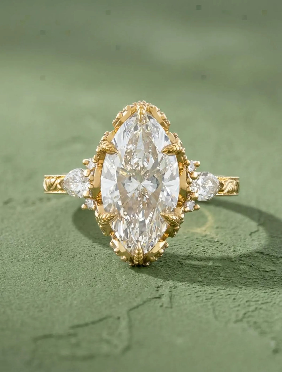 Top view of a 4 CT marquise cut lab grown diamond engagement ring in yellow gold featuring claw prongs, pear side stones, and an engraved band.