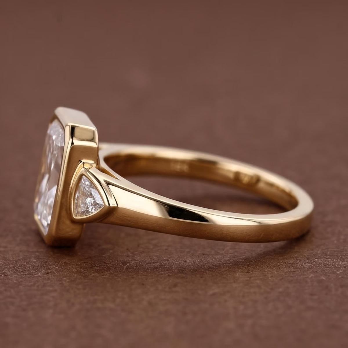 Side angle view of a 5 CT radiant cut lab grown diamond engagement ring in a yellow gold bezel setting with trillion side stones.