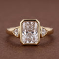 Top view of a 5 CT radiant cut lab grown diamond three-stone ring with bezel-set trillion side diamonds in yellow gold.