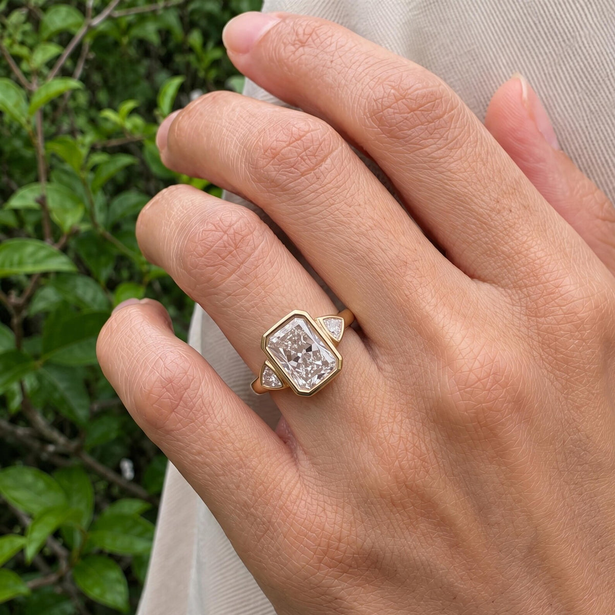 On-hand view of a 5 CT radiant cut lab grown diamond three-stone bezel engagement ring in natural light.