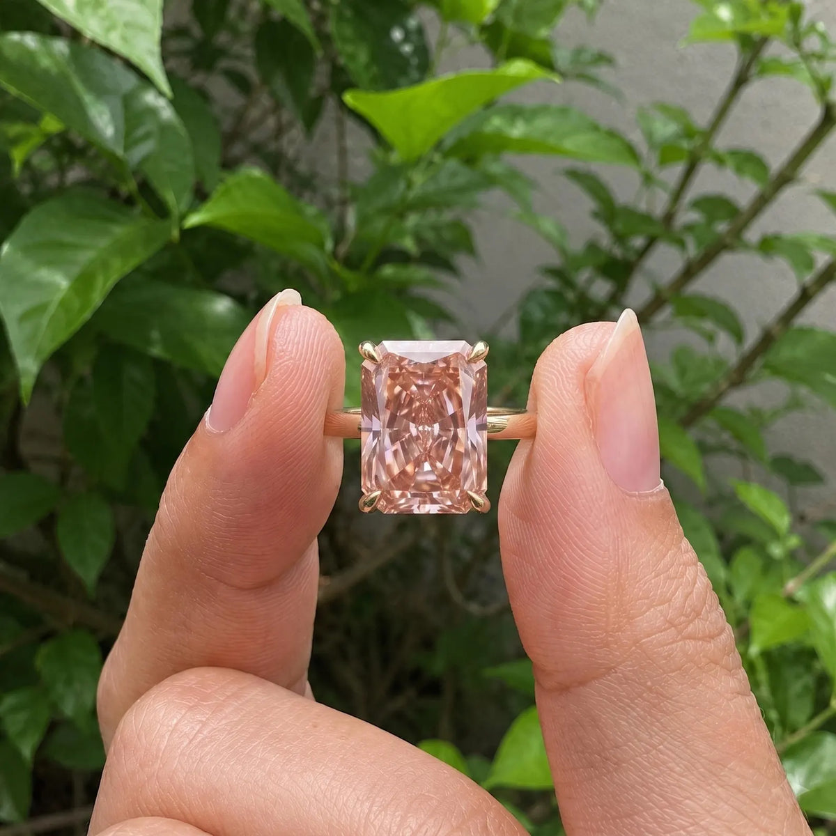 Close-up view of a 4 CT fancy pink radiant cut lab diamond solitaire held between fingers in natural light.