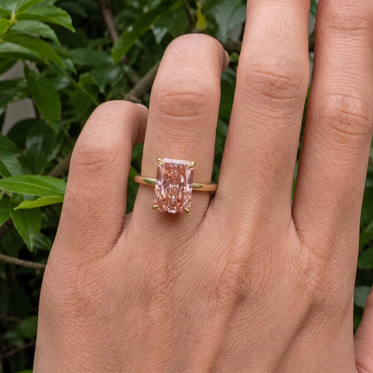 Top-down close-up view of a 4 CT fancy pink radiant cut lab diamond ring on hand.