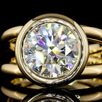 Extreme close-up of a 4 CT brilliant round cut lab grown diamond encased in a thick yellow gold full bezel frame.