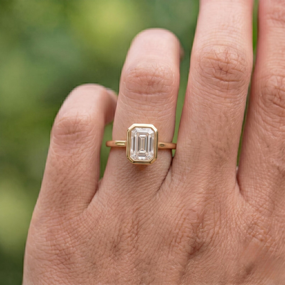 2 CT emerald cut lab grown diamond bezel solitaire ring worn on hand in natural lighting.
