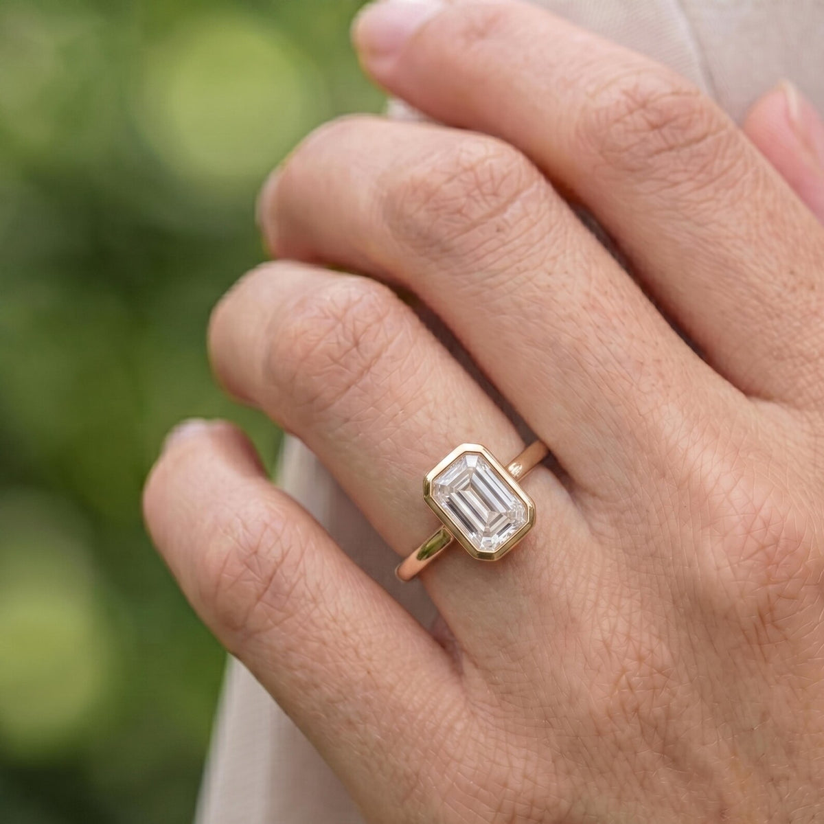 Angled perspective of a 2 CT emerald cut lab diamond bezel ring on finger showing step-cut facets.