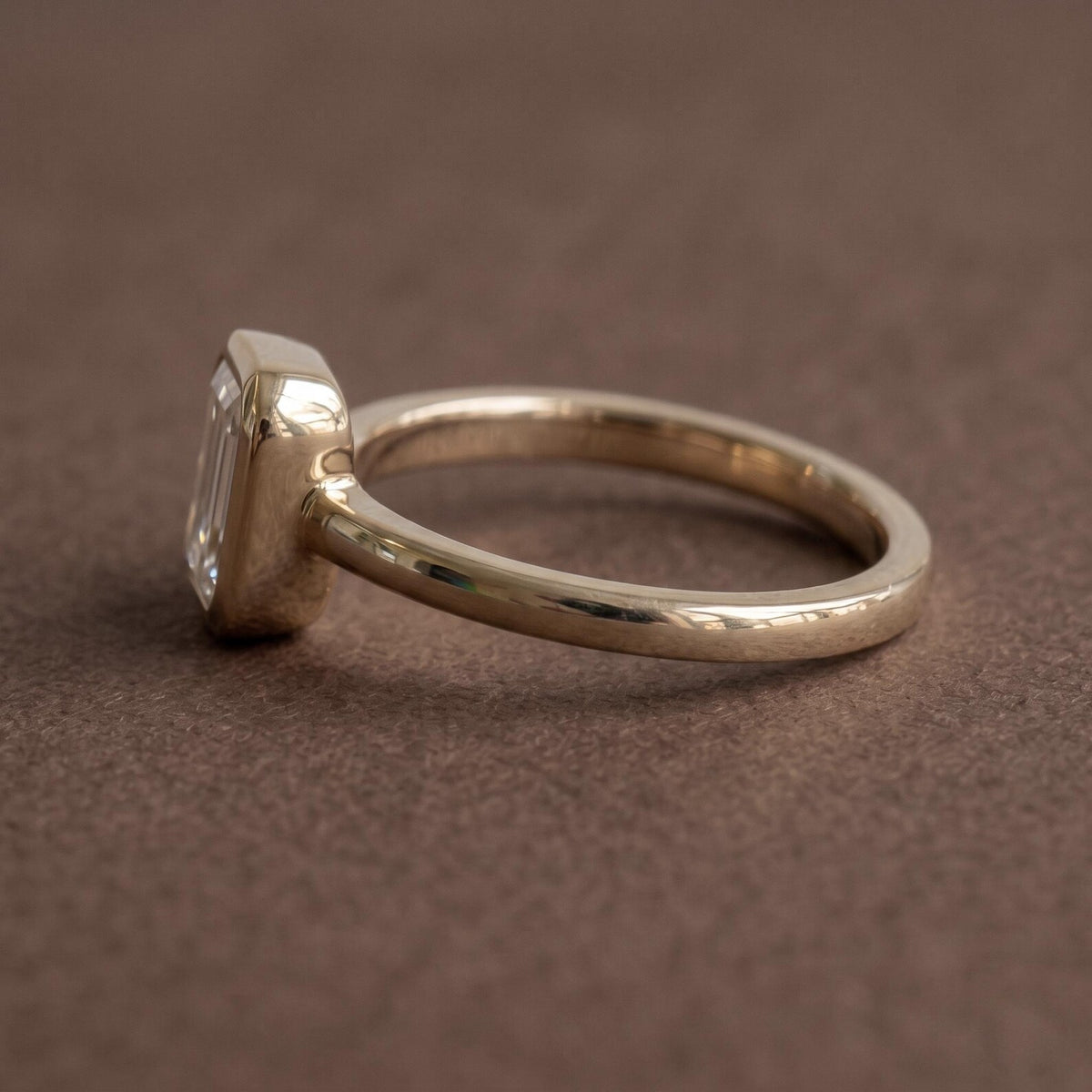 Side profile view showing the low-profile bezel setting and smooth rounded gold band of a 2 CT emerald diamond ring.