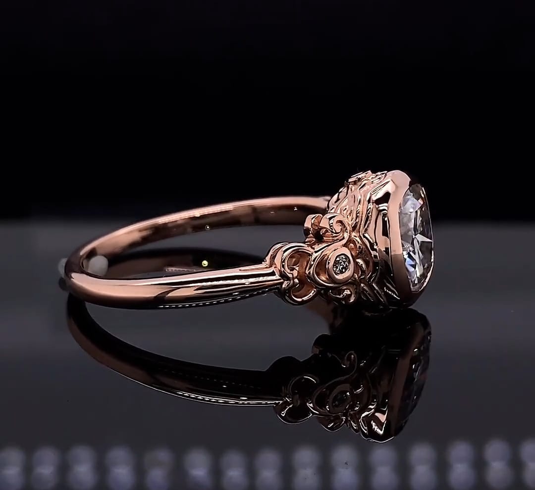 Side profile view of a vintage rose gold engagement ring showing intricate filigree details and a bezel-set cushion cut lab diamond.