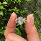 Close-up view of a 3 CT oval lab diamond ring with botanical leaf accents held between fingers.