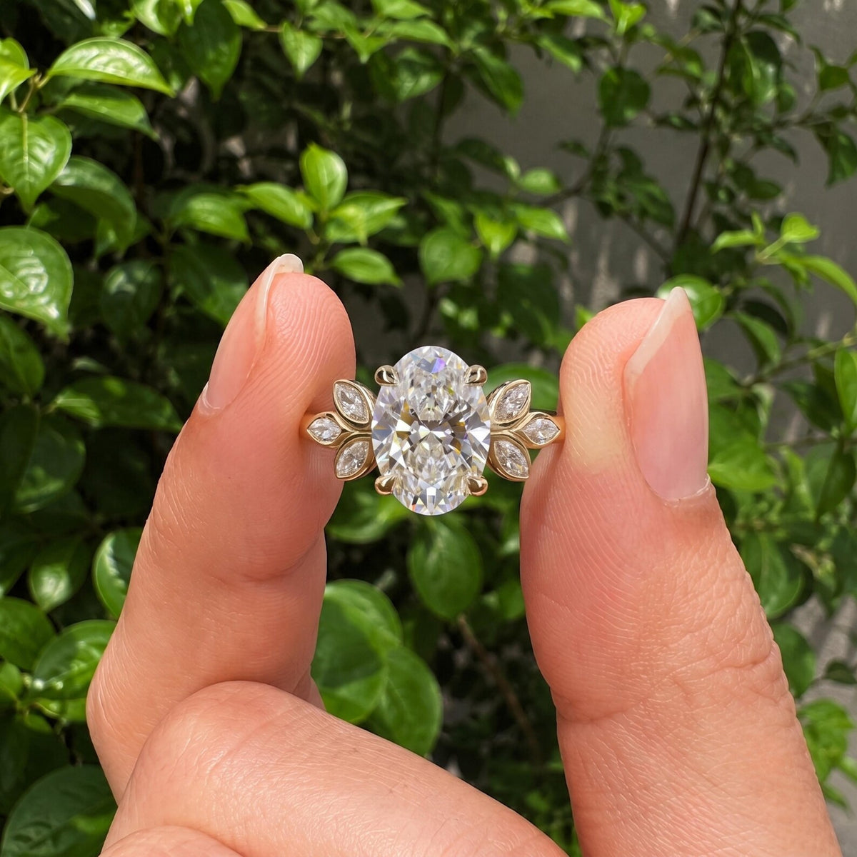 Close-up view of a 3 CT oval lab diamond ring with botanical leaf accents held between fingers.