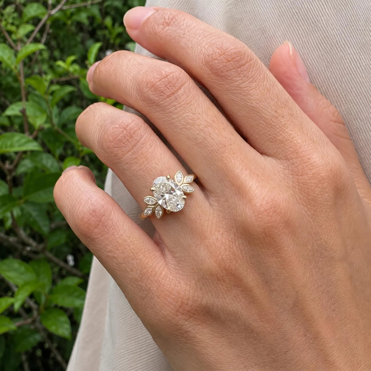 3 CT oval cut lab grown diamond ring with marquise cluster sides styled on hand in natural lighting.