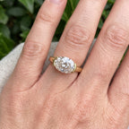 Close-up view of a 3 CT East-West oval lab grown diamond ring with half-bezel setting in yellow gold on finger.