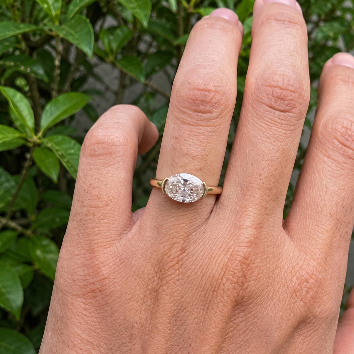 Natural light view of a modern 3 CT East-West oval lab diamond half-bezel engagement ring.