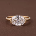 Studio shot of a 3 CT oval lab diamond set horizontally in a yellow gold half-bezel setting.