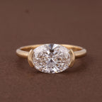 Studio shot of a 3 CT oval lab diamond set horizontally in a yellow gold half-bezel setting.