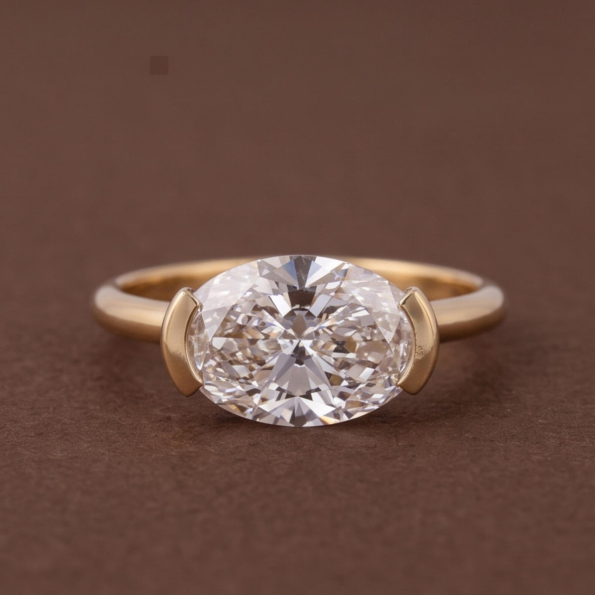 Studio shot of a 3 CT oval lab diamond set horizontally in a yellow gold half-bezel setting.