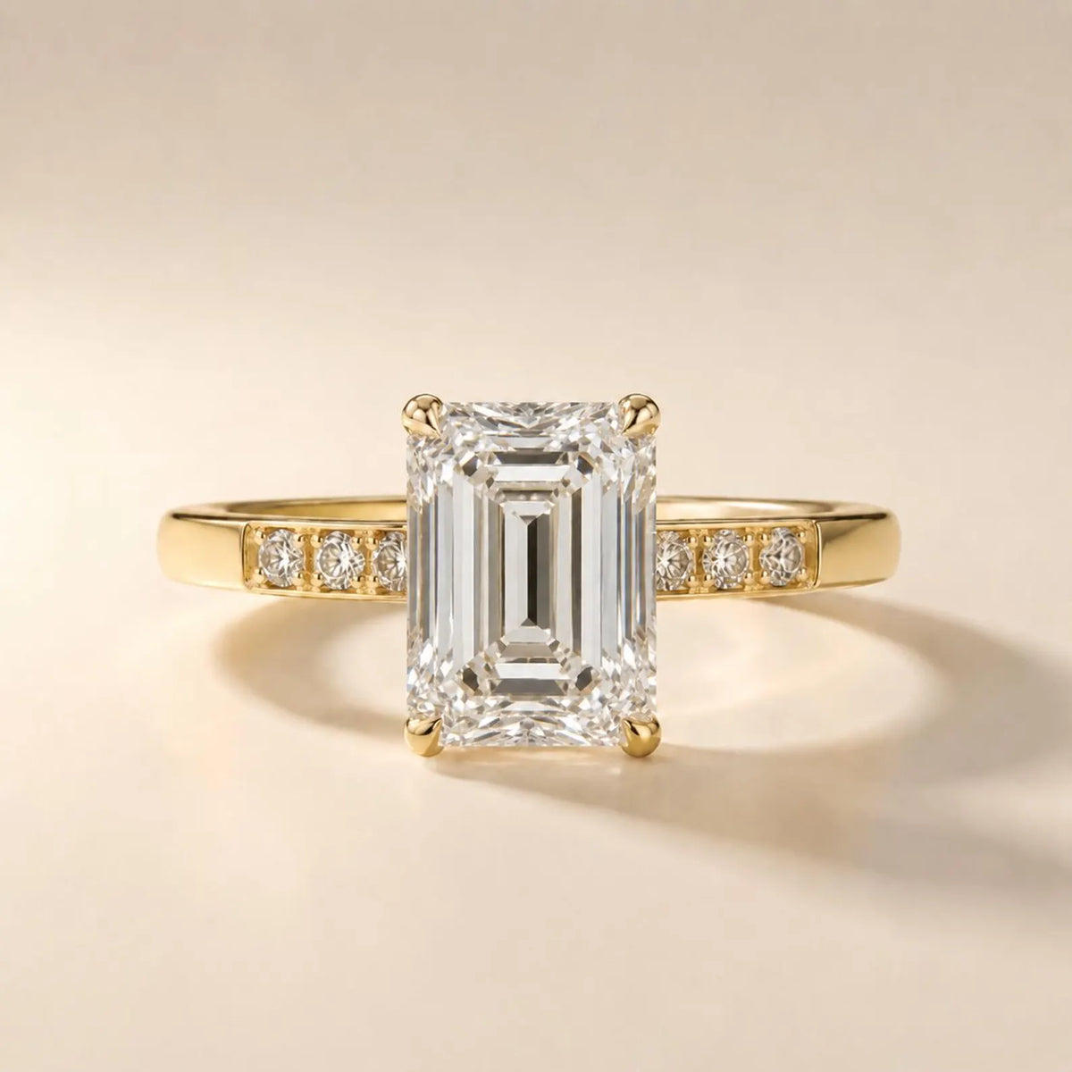 Front view of a 4 CT emerald cut lab grown diamond engagement ring with round channel-set accents on a yellow gold band.