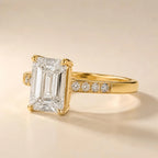 Angled side profile showing step-cut clarity of a 4 CT emerald cut lab diamond and channel-set accent stones in yellow gold.